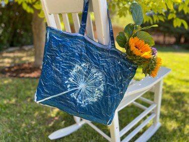 Solar print of an allium on a tote bag filled with flowers hanging on a white rocking chair in the backyard
