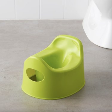 Lime green plastic toddler potty sitting on the floor of a bathroom.