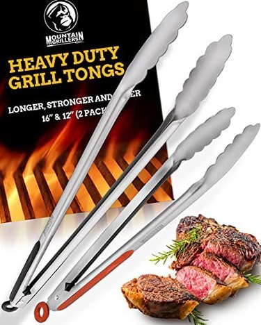 Twin-pack of Mountain Grillers tongs, pictured against their packaging on a white ground, with an image of a sliced, cooked steak in the bottom left corner