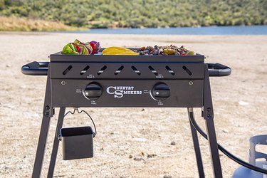 Compact Country Smokers flat top grill, depicted on a beach with vegetables, meats and tortillas on the cooking surface