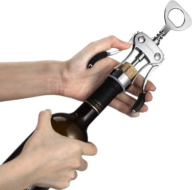 Beneno wine opener, pictured in the act of opening a bottle of wine, on a white ground