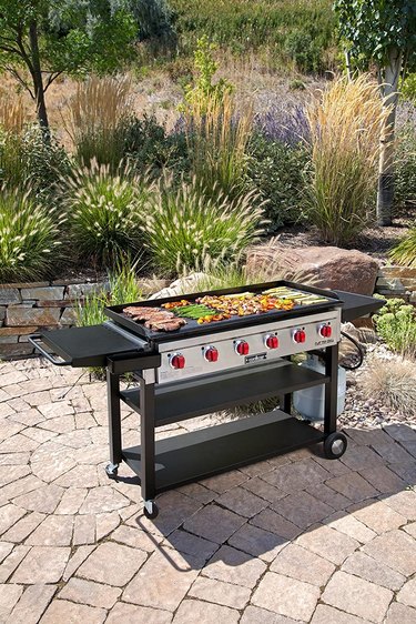Camp Chef 900 Flat Top Grill on a stone patio, being used to cook meat and vegetables.