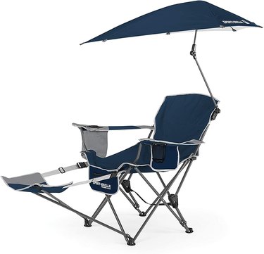 Sport-Brella Beach Chair with Umbrella against a white background. The chair and umbrella are a dark blue and the zippered storage pocket and foot rest are mostly gray.