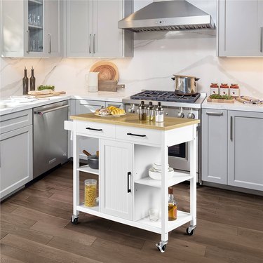 Yaheetech kitchen island cart, in white, depicted in a modern white kitchen with wood floors and stainless steel appliances