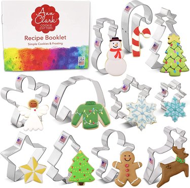 Set of Ann Clark Christmas-themed cookie cutters displayed on a white ground, with a decorated cookie in front of each cutter, and the accompanying recipe booklet shown in the top left corner