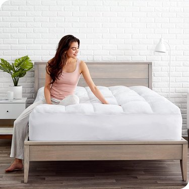 Woman sitting on a very fluffy white mattress topper on a wood-frame bed.