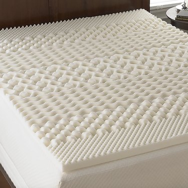White mattress topper on bed with various egg-crate like textures that mark the different support zones.