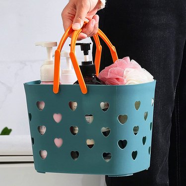 Teal shower caddy made of a silicone-like material with perforated hearts and orange plastic handles.