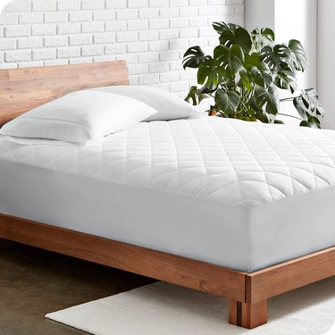 White mattress topper on a wood frame bed. It has a quilted texture but doesn't look overly fluffy.