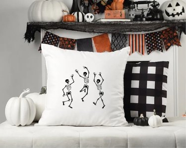 Dancing skeletons Halloween throw pillow from Etsy. The pillow here is white with three black skeletons dancing.