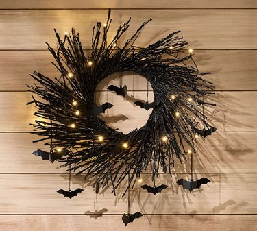 Pre-Lit Black Glitter Branch Wreath with Bats from Pottery Barn against a wood wall.