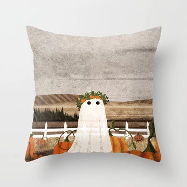 Halloween throw pillow with a ghost from Society6. The ghost is cartoon-ish and standing in a pumpkin patch. The sheet-like ghost is wearing a flower crown and only has eyes.