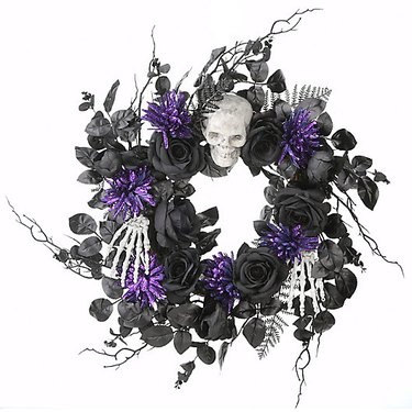 Halloween Wreath in Purple/Black with Skull and Flowers from Bed Bath & Beyond against a white background. In addition to a skull there are skeleton hands on it.