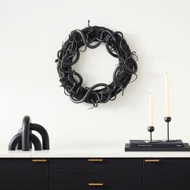 Black grapevine wreath with rubber snakes all around it above a credenza with black and white accessories.