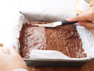 Using an offset spatula to spread brownie batter in pan.