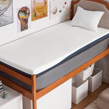 4-inch memory foam mattress topper on a raised dorm bed with a small headboard and boxes under the bed.