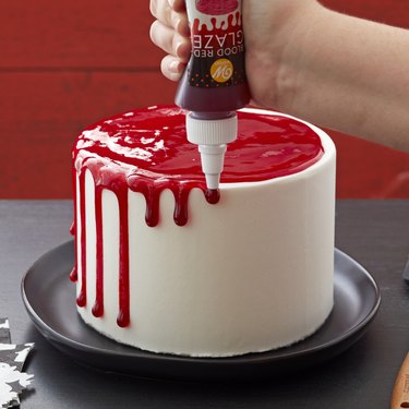Edible Fake Blood Glaze from Walmart in a squeeze bottle, being dribbled down the side of a white cake to create a dripping blood effect.