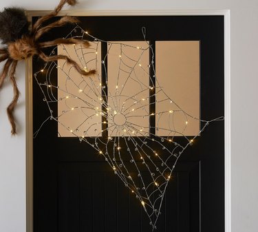 Lit Crystal Spider Web from Pottery Barn Spread Across a Front Door With a Faux Giant Spider in the Corner.