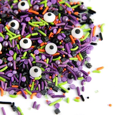 Halloween-themed sprinkles in green, orange, purple, and black with candy eyeballs and different sized/shaped sprinkles.