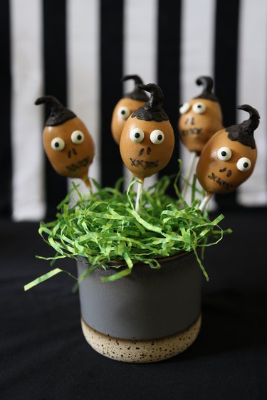 "Beetlejuice" shrunken head cake pops displayed in a jar with green paper grass