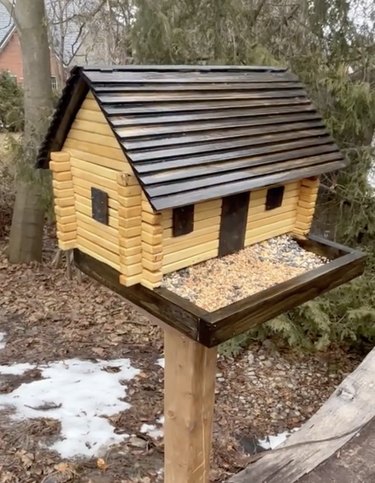 Wood birdhouse shaped like a rustic log cabin on a large wooden stand