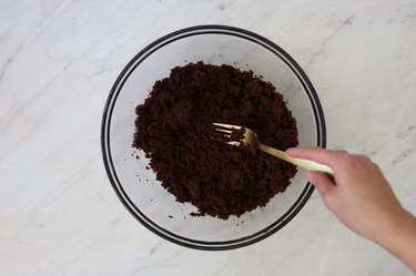 Crumbling a chocolate cake with a fork in a glass mixing bowl