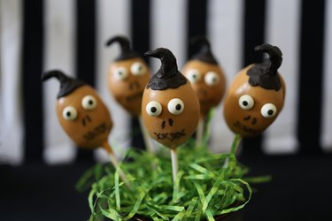 "Beetlejuice" shrunken head cake pops displayed in a jar with green paper grass