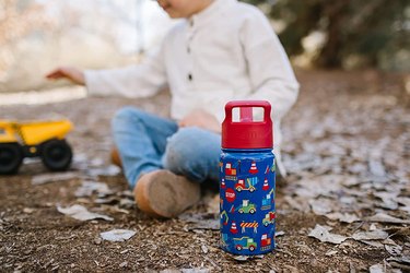 Child sitting in dirt next to red and blue water bottle