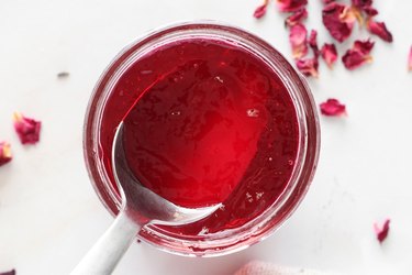 Rose petal jelly in jar surrounded by petals