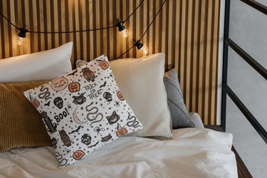 Cartoon-style Halloween throw pillow on a daybed surrounded by string lights and coordinating throw pillows.