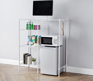 White wire shelving unit that goes over a mini fridge and has four total shelving surfaces.