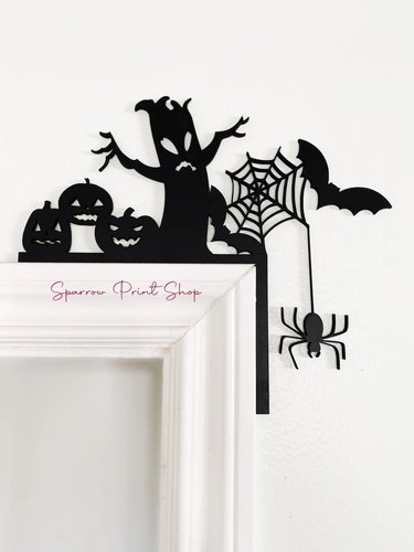 Spiderweb & Pumpkins Door Corner from Etsy. It sits over the top edge of the door and features a spooky looking tree and a dangling spider.