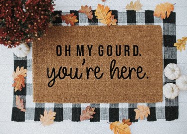Coir doormat on a black and white rug that reads "Oh my gourd, you're here"