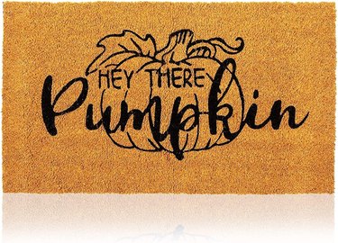 Hey There Pumpkin coir doormat. Hey There is written in all caps and pumpkin is in a script-like font. It's against the outline of a pumpkin on a vine with a leaf.