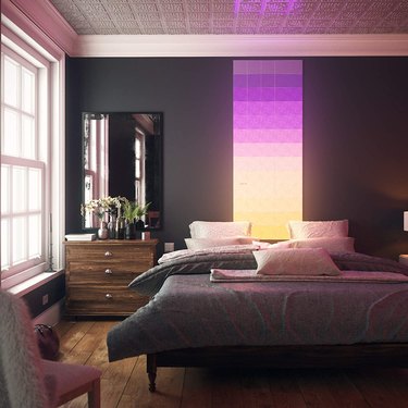 Bedroom with dark walls that features a wide strip of LED panels behind it that light up in different colors.