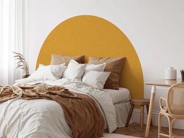Headboard decal in mustard yellow behind a queen-size bed with lots of linen bedding. The decal has a fabric-like texture.