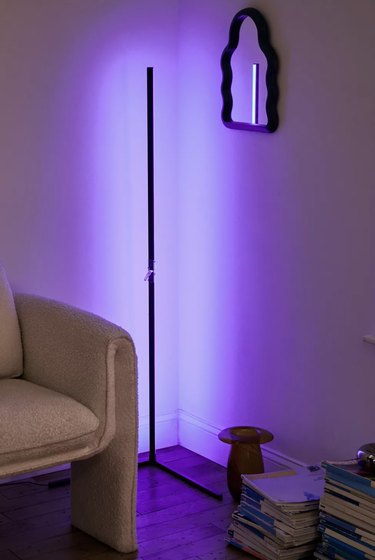 A color-changing corner floor lamp bouncing dim, purple light into a living room. The lamp is very thin and 55 inches tall.