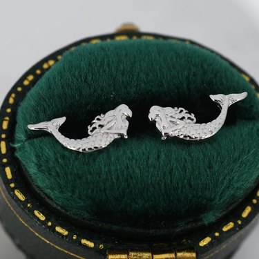 Silver mermaid stud earrings on green fabric