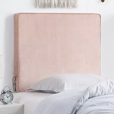 A light pink, rectangular twin XL headboard in a velvety fabric with small pockets on either side for holding a phone or keys.