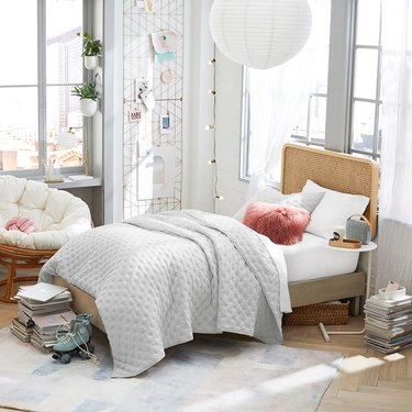 Cane headboard shown on a twin-sized bed in a dorm room with lots of cute decor like a paper lantern and a papasan chair.