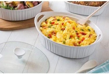 Corning 2.5 quart French White oval casserole, shown holding a colorful pasta dish on a rustic tabletop, with other French White dishes visible in the background