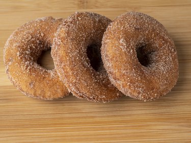 Three apple cider donuts on a wood surface