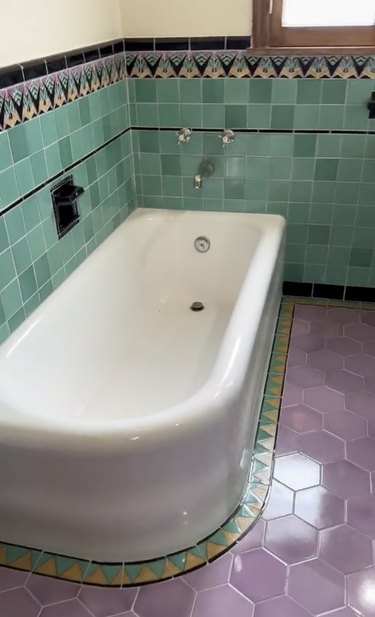 Bathroom with purple tile flooring, turquoise wall tile and a white bathtub