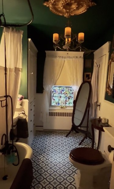 Bathroom with dark green walls, black-and-white tile flooring and a gold chandelier