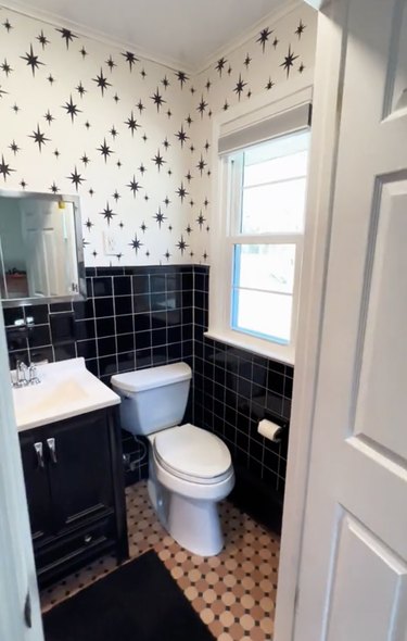 Bathroom with black tile walls, black-and-white starburst wallpaper and a peach tile floor