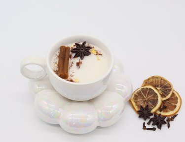 White candle in a white mug with wax cinnamon stick and star anise