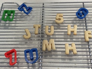 Alphabet cookies and cutters cooling on wire rack.