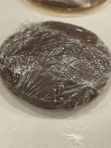 Chocolate layer cake covered in plastic wrap.