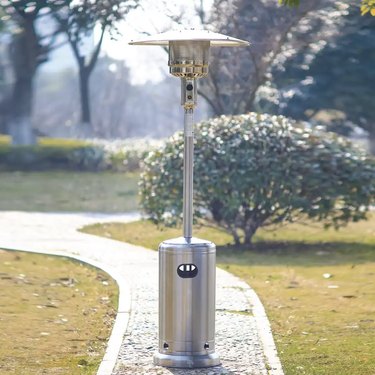 7-foot stainless steel patio heater on a sidewalk in front of a bush