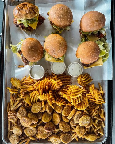 A bird's-eye view of a platter filled with two rows of three smash burgers, dipping sauce and an overflowing pile of fries and fried jalepenos.